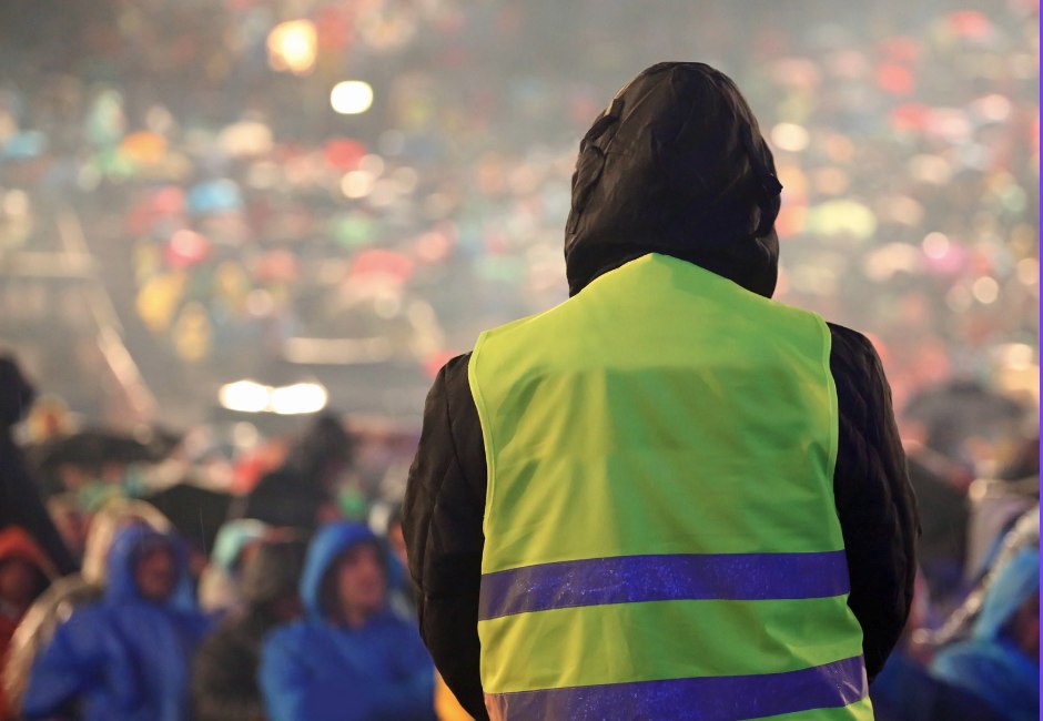 Sicherheitskraft mit Warnweste vor dem Publikum einer Veranstaltung