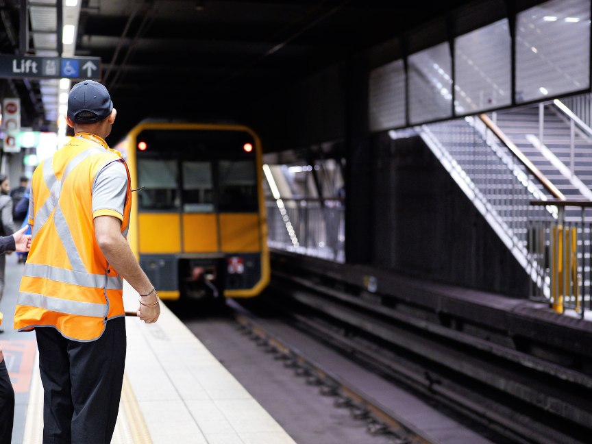 Sicherheitskraft mit Warnweste auf einem Bahnsteig vor einfahrendem Zug