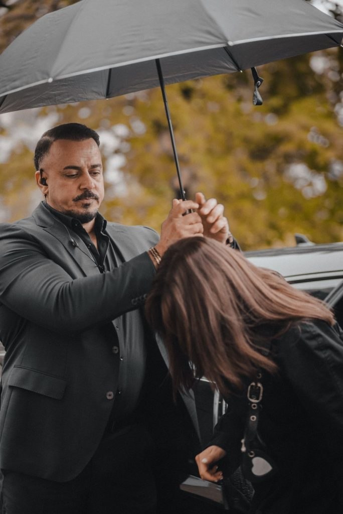 Personenschützer begleitet eine Frau mit Regenschirm zum Fahrzeug